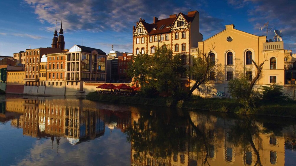 A river reflecting buildings, including a church with spires and a traditional house with a sloped roof. 1