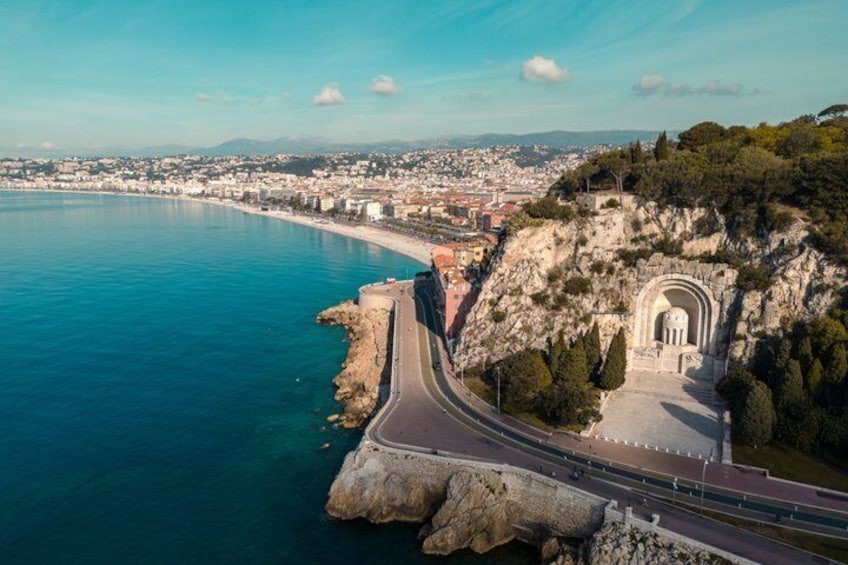 A coastal cityscape with a prominent cliff, a road curving along the coastline, and a historical building with an arched entrance. 3