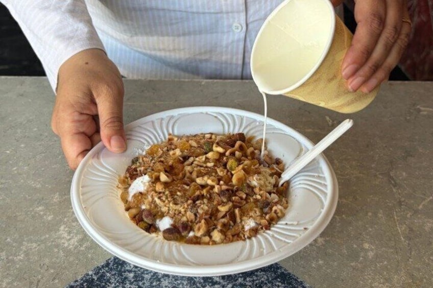 A person pouring milk into a bowl of cereal with nuts and raisins. 2