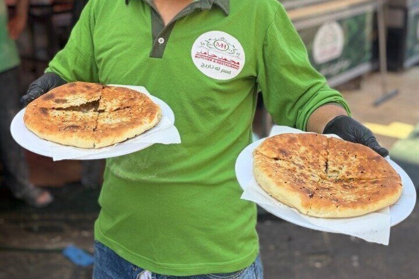 A person in a green shirt holding two round flatbreads on plates. 4