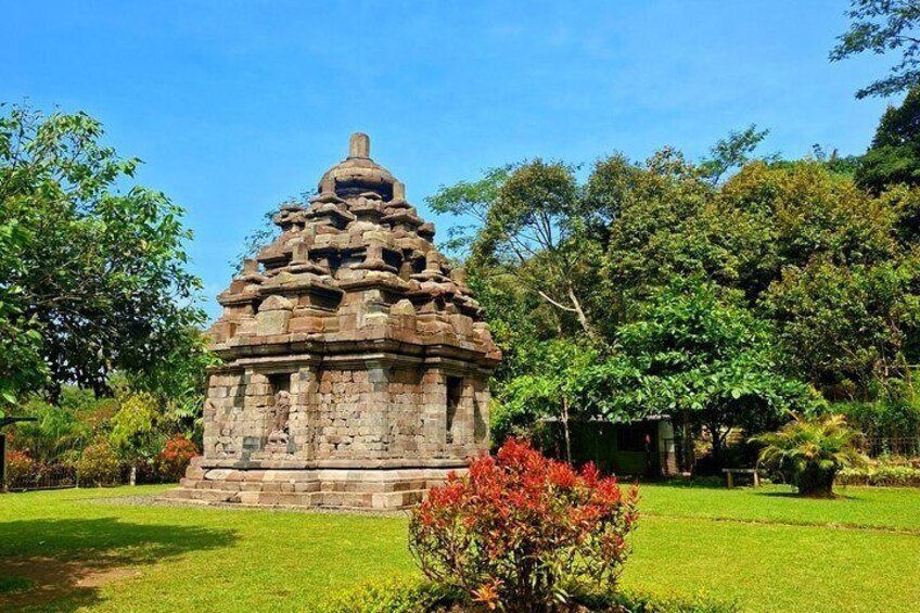 A stone temple with a tiered roof, surrounded by lush greenery and trees. 1