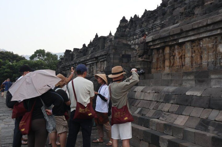 A group of tourists observing ancient stone carvings on a temple wall. 4