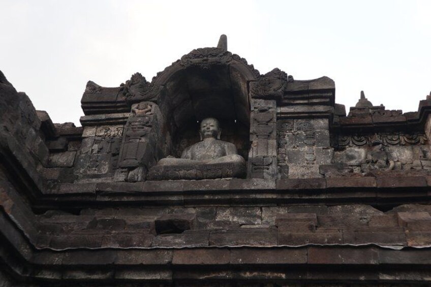 A stone structure with a central seated figure, possibly a statue, surrounded by intricate carvings and architectural details. 2