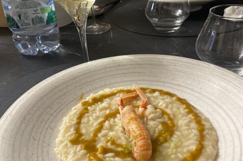 A plate of risotto with shrimp and a green sauce, a water bottle, and a glass of white wine on a table. 2