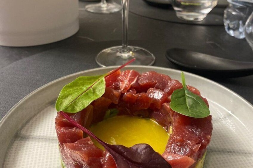 A plate with a food item, garnished with a leaf, and a glass of wine in the background. 5