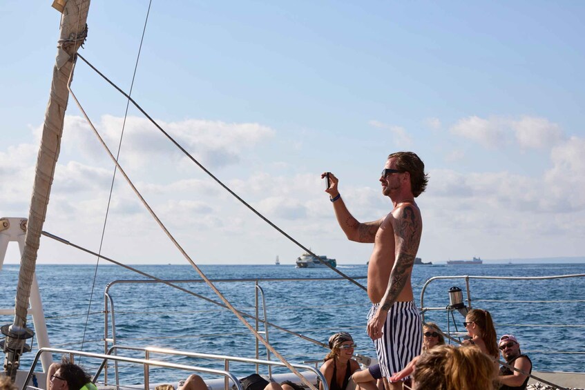 A man standing on a boat with a tattoo, holding a camera, and a group of people below him. 4