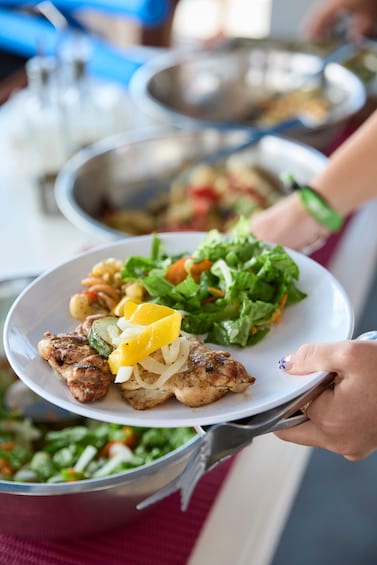 A person holding a plate with grilled chicken, vegetables, and a salad. 2