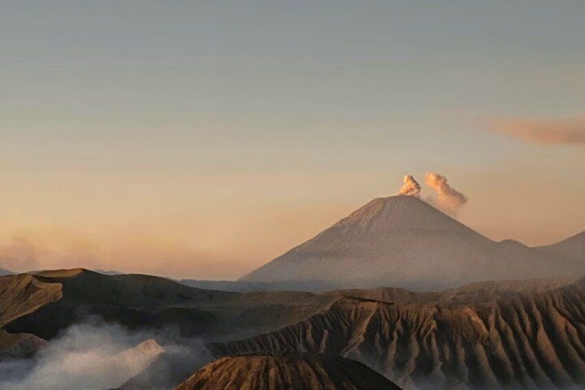 A mountain with smoke, a valley, and a clear sky. 3