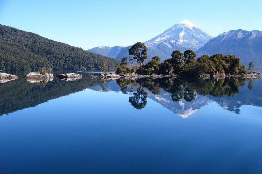 A calm lake with clear reflections, a forested island, and a snow-capped mountain in the background. 3