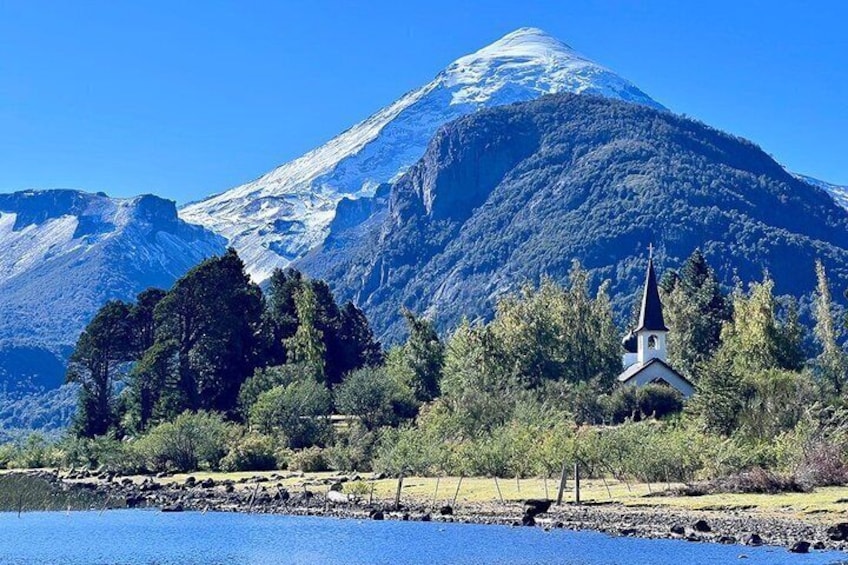 A church surrounded by trees and a mountain with snow. 1