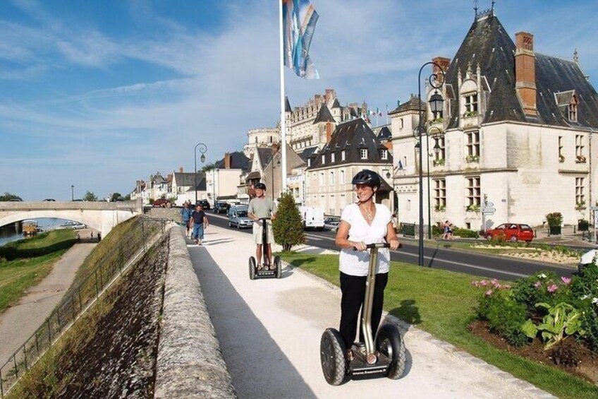 A person riding a Segway on a paved path, a canal, and historic buildings in the background. 3