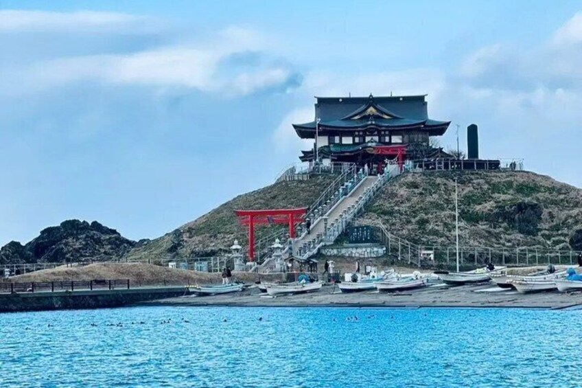 A traditional Japanese building with a red torii gate, a staircase leading up to it, and boats in the water. 5