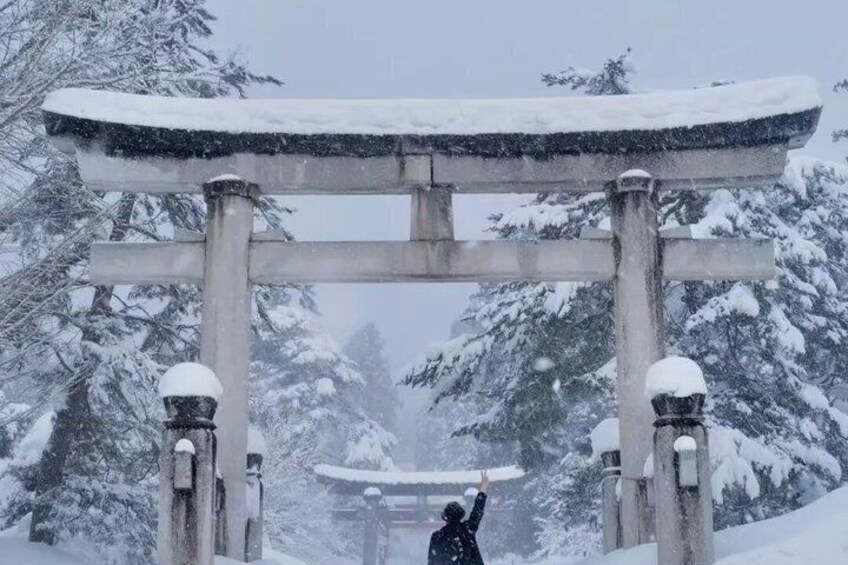 A snow-covered torii gate with a person raising their hand. 1