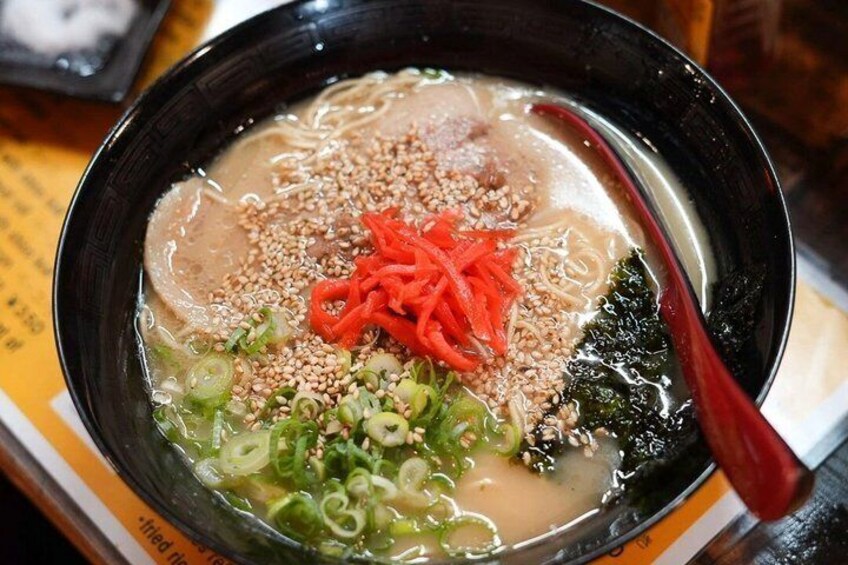 A bowl of soup with noodles, green onions, sesame seeds, and red chili peppers. 3