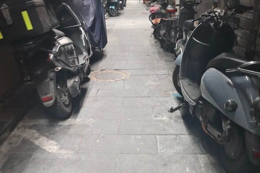 A narrow alley with parked scooters and a three-wheeled vehicle. 2