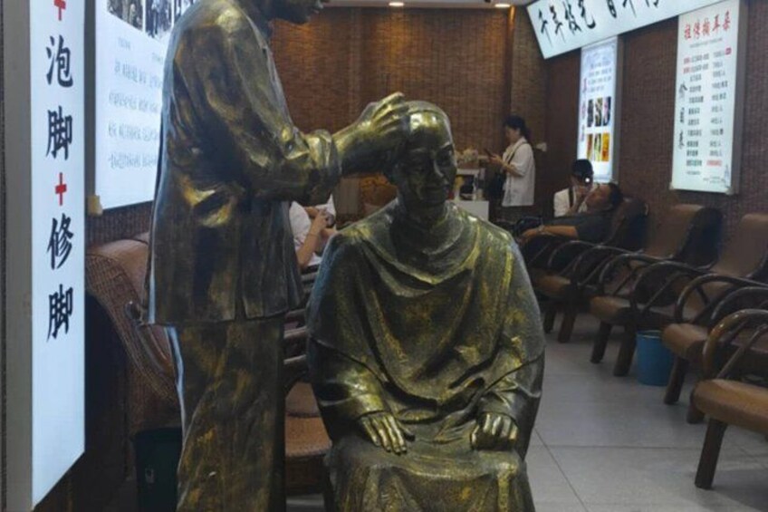 A statue of a person in a medical setting, possibly a clinic or hospital, with chairs and a counter in the background. 4