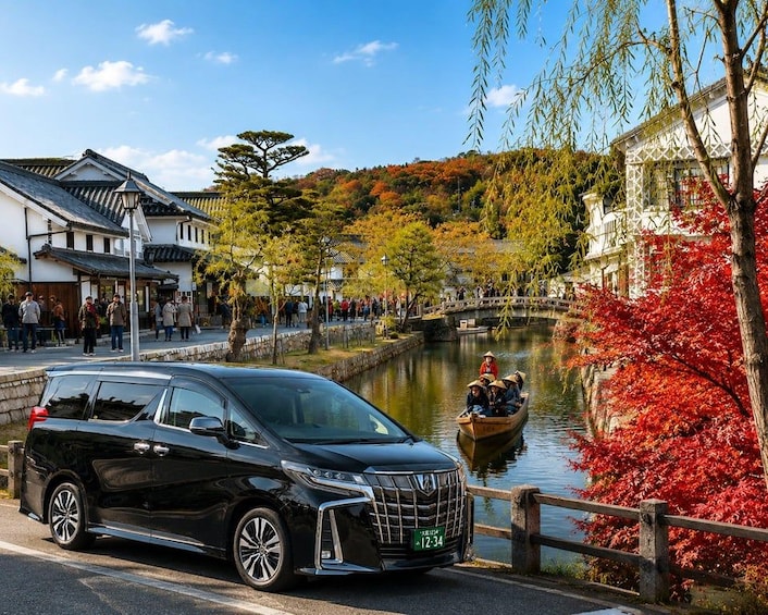 A black minivan parked by a river with a traditional Japanese building and a bridge in the background. 2