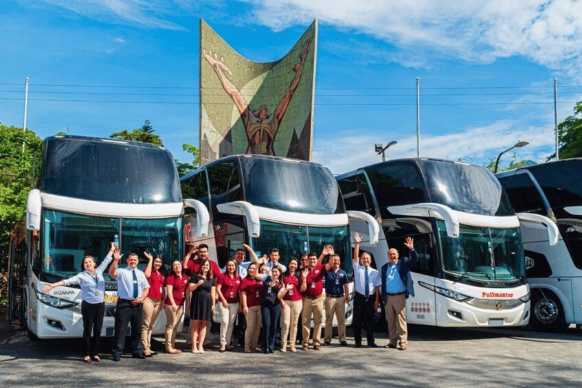 A group of people standing in front of three buses with a large flag in the background. 3