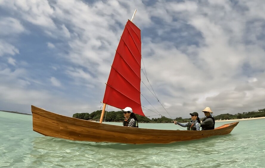 A wooden boat with a red sail on clear turquoise water. 4