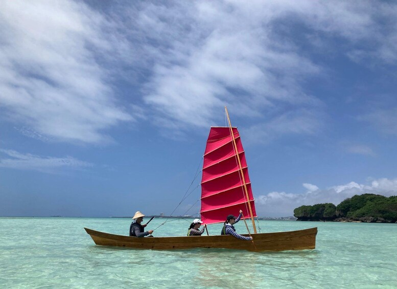 A traditional wooden boat with a red sail on clear turquoise water, surrounded by a calm sea and a cloudy sky. 1