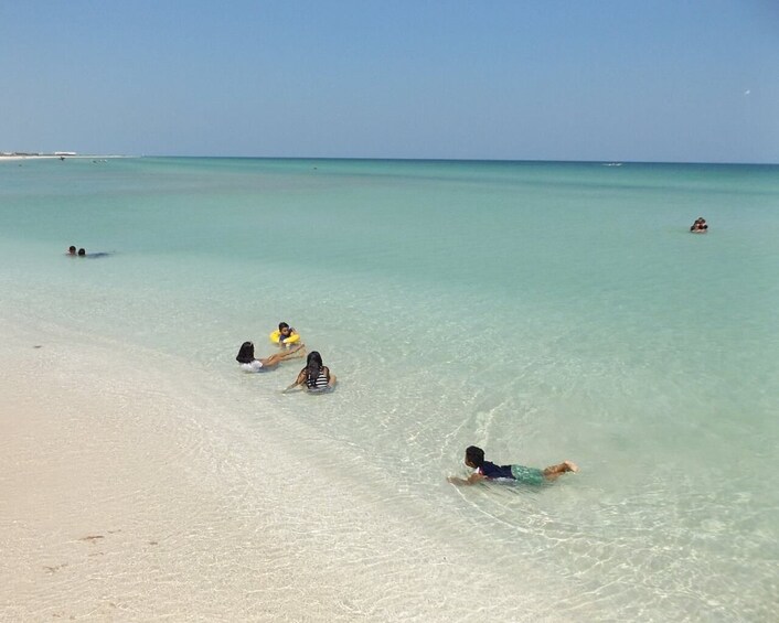 A beach with clear turquoise water, people swimming and sunbathing. 5