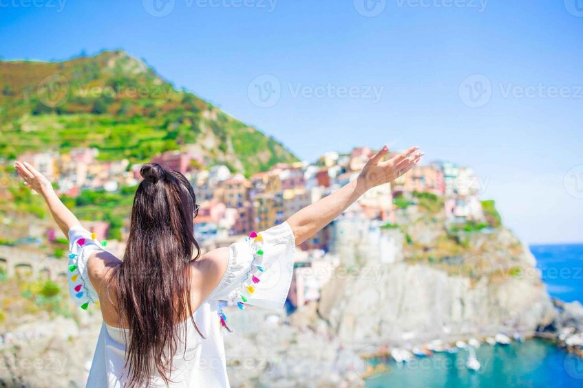 A person with arms outstretched facing a coastal town with buildings on a cliff. 1