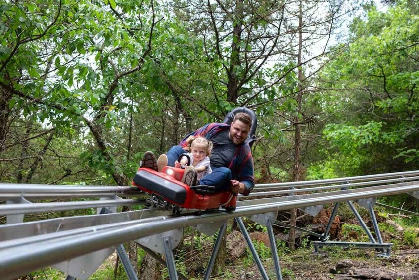 A person and a child on a red amusement ride in a wooded area. 2