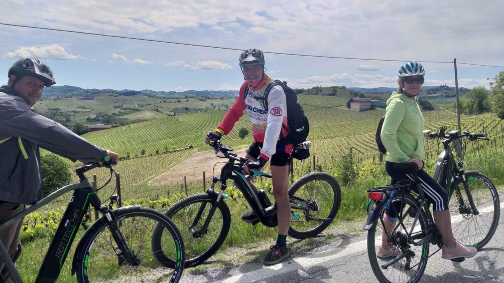 Three cyclists on a road with vineyards in the background. 3