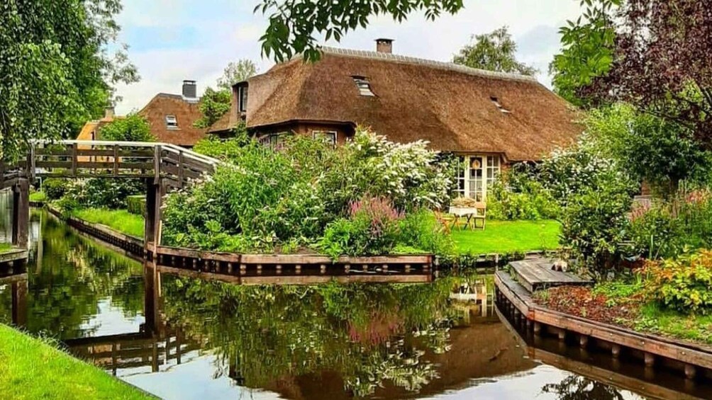 A canal with a house reflecting on the water, surrounded by greenery and a wooden bridge. 2
