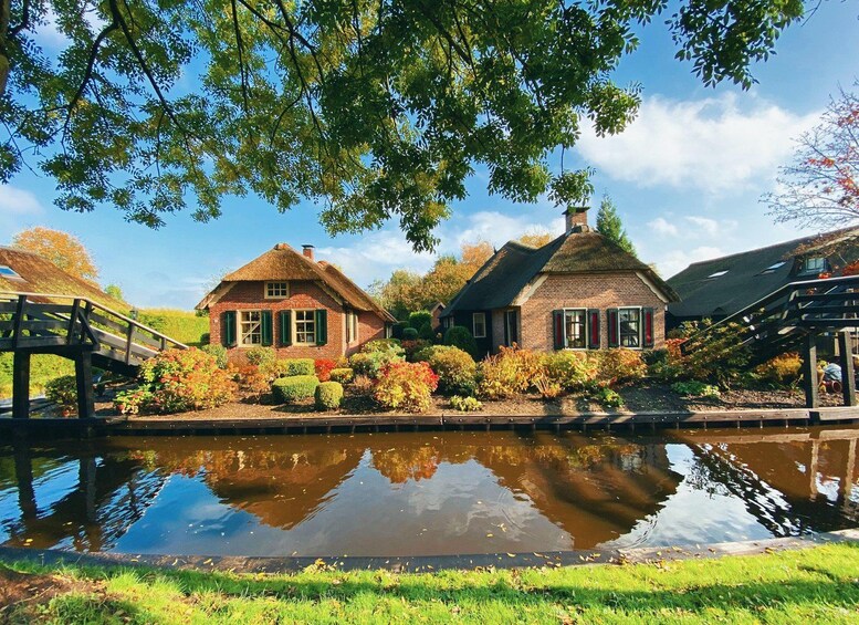 A canal with two thatched-roof houses, a wooden bridge, and lush greenery. 5