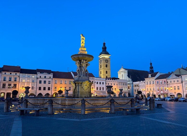 A historic square with a prominent fountain, a clock tower, and classical architecture. 2