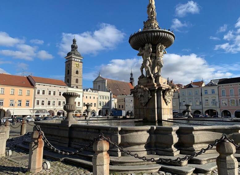 A historic fountain with statues, a clock tower, and traditional buildings in the background. 1