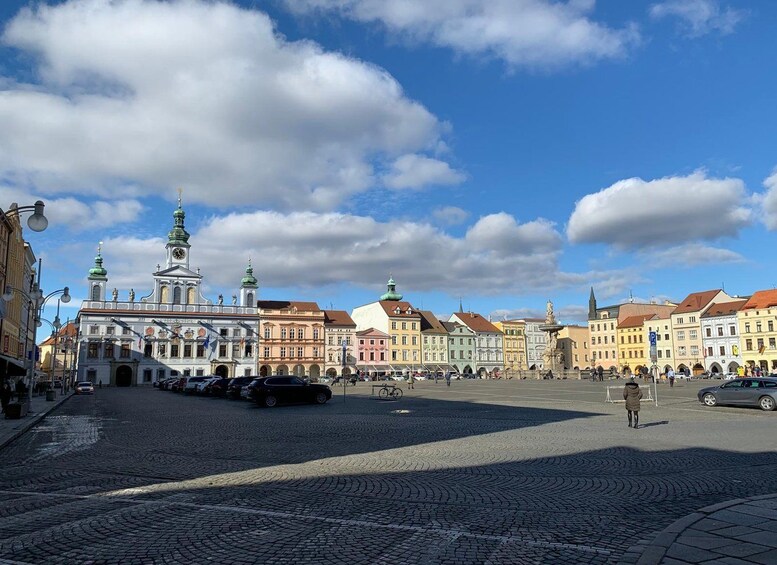 A cobblestone square with historic buildings, a prominent church with a clock tower, and a clear blue sky with clouds. 5