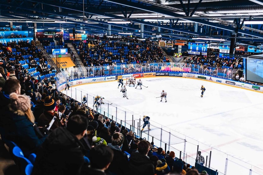 An indoor ice hockey rink with players, spectators, and advertisements. 3