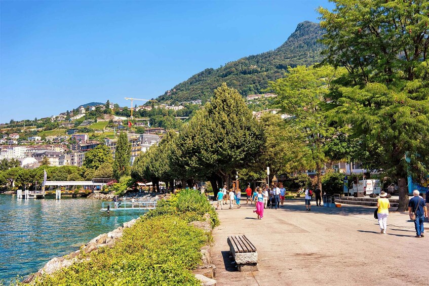 A lakeside promenade with people walking, a dock, and a mountain in the background. 4