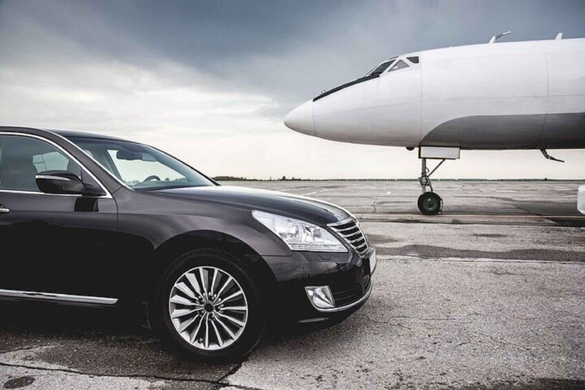 A black car parked on an airport tarmac with a large airplane in the background. 5