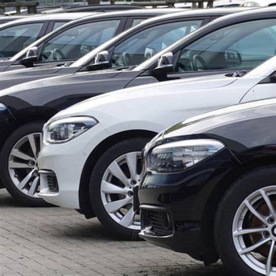 A row of parked cars, predominantly white and black, with visible wheels and side mirrors. 1