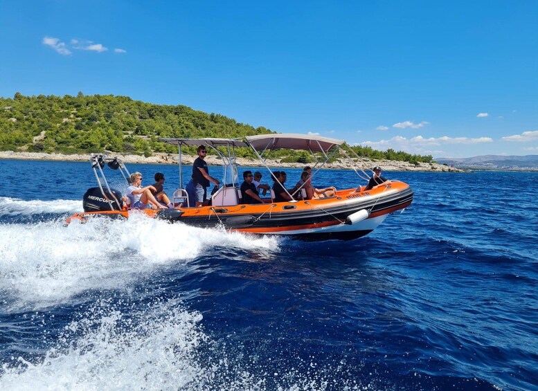 A group of people on an orange and black inflatable boat speeding across a blue body of water. 1