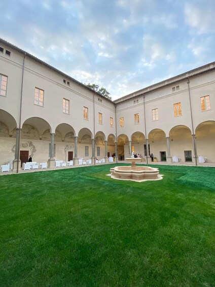 A courtyard with a fountain, green lawn, and a building with arches and columns. 5