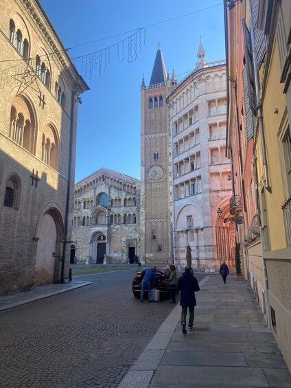 A cobblestone street with historic buildings, a clock tower, and a person walking. 1
