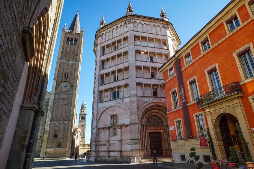 A historic square with a prominent clock tower, a central building with classical architecture, and a red building with a balcony. 4