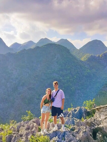 Two people standing on a rocky outcrop with a mountainous landscape in the background. 3