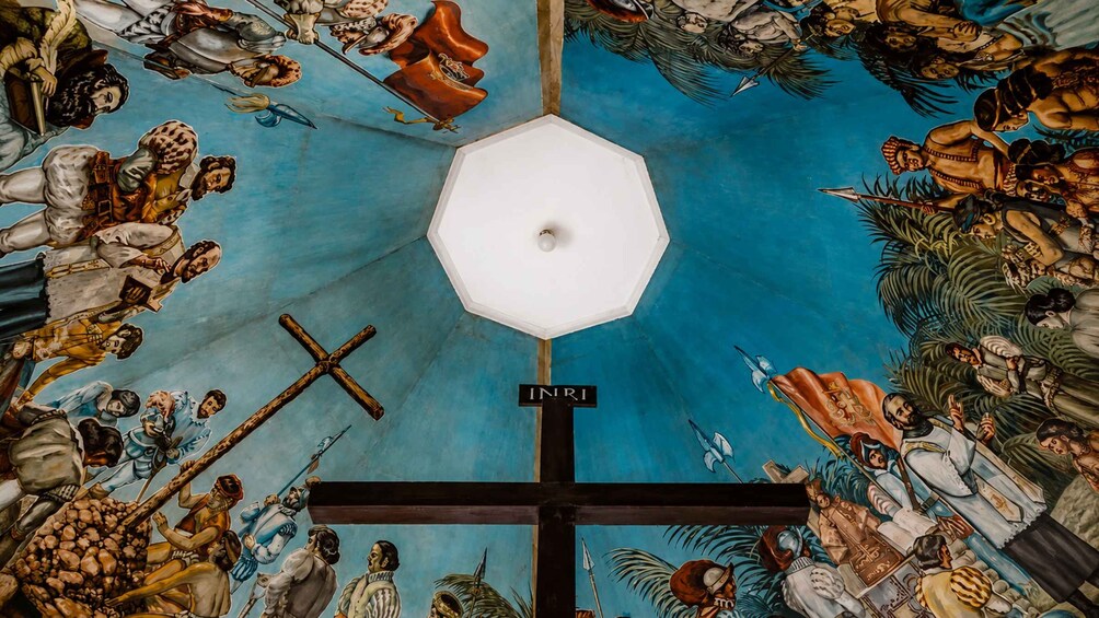 A ceiling mural with a cross, surrounded by figures in various poses and attire. 5