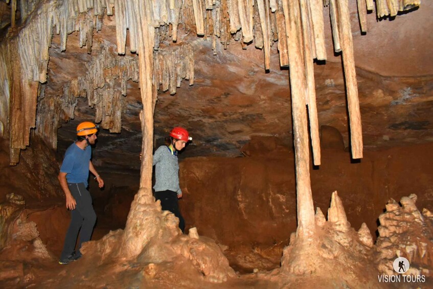 Two people exploring a cave with stalactites and stalagmites. 1