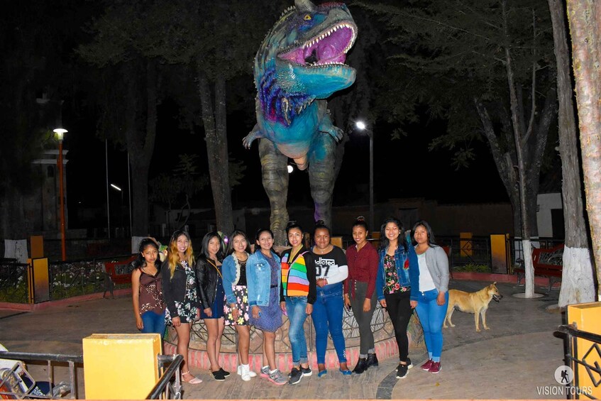 A group of people posing in front of a large dinosaur statue. 2