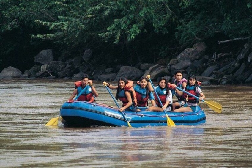 A group of people in a blue raft on a river surrounded by rocks and greenery. 1
