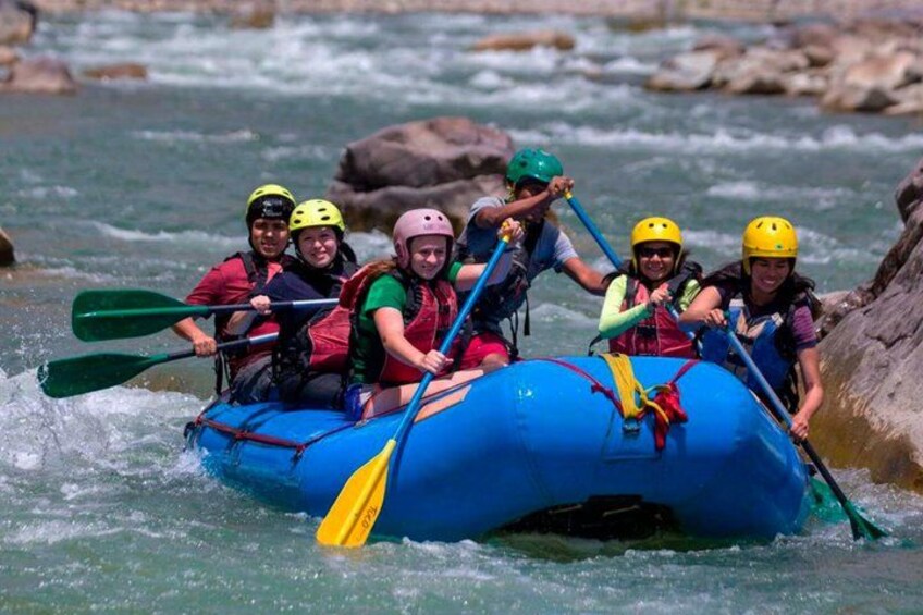 A group of people rafting on a blue inflatable raft in a river with rocks. 2