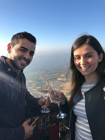 Two people holding wine glasses with a scenic landscape in the background. 3