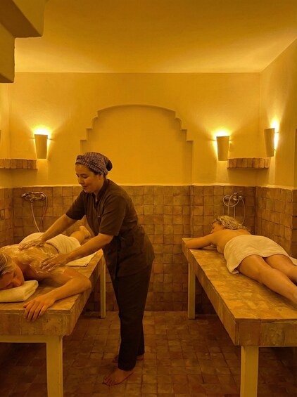A spa with two massage tables, a masseuse attending to a client, and a second client resting. 5