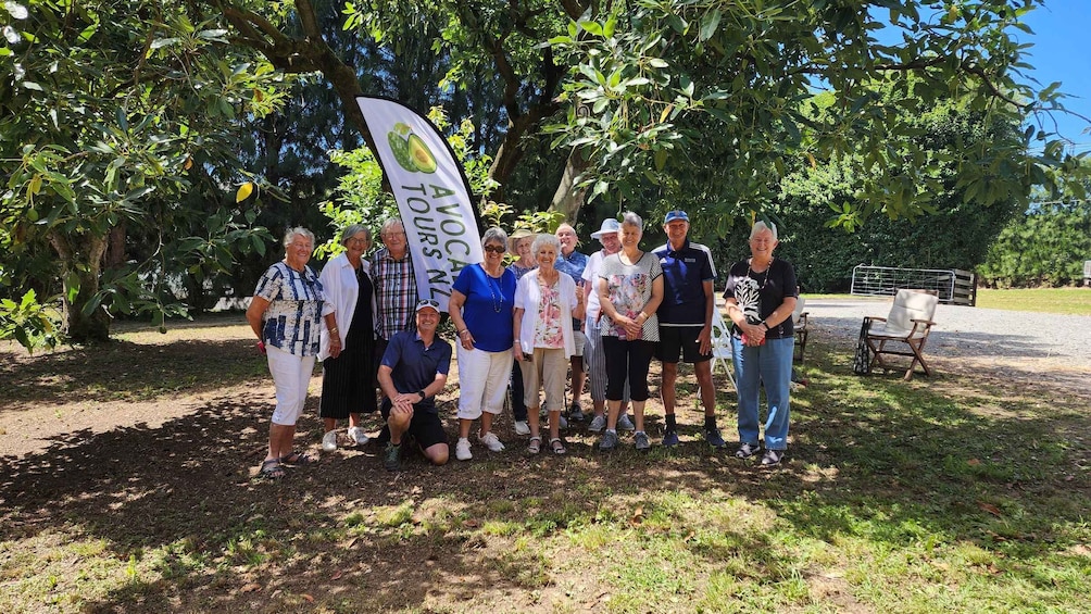 A group of people posing in a park with trees and a banner. 2